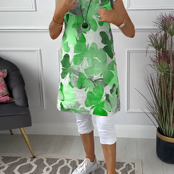 
A sleeveless summer tunic top for women featuring a vibrant floral print. The top is displayed in a standing position, highlighting its chic design suitable for fashionable summer wear. The background includes accents of green and white, complementing the floral theme.