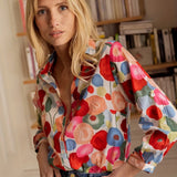 Blouse made of floral silk fabric in vibrant spring colors, featuring a dress shirt style with a focus on the shoulder and neck area, paired with jeans.