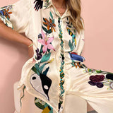 Women's floral silk blouse with designer patterns, featuring a white base color, dress shirt style with a collar, long sleeves, and a fitted waist, showcasing elegant fashion.