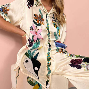 Women's floral silk blouse with designer patterns, featuring a white base color, dress shirt style with a collar, long sleeves, and a fitted waist, showcasing elegant fashion.