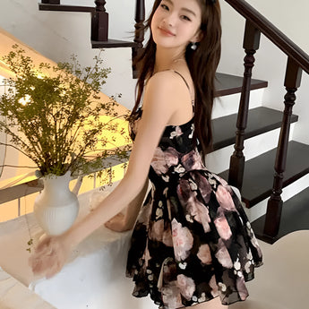 A woman wearing a floral strapless mini dress, posing elegantly in a black party wear outfit, in a flash photography setting.