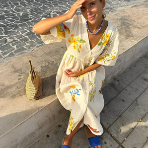 Woman wearing a floral summer dress with embroidery, smiling while enjoying a leisurely day outdoors, accessorized with sunglasses.