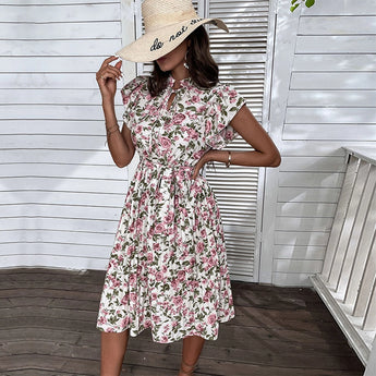 Alt Text: Woman wearing a white floral summer midi dress with short sleeves and an A-line cut, featuring a tie waist. She is accessorized with a hat and eyewear. The dress is designed for a 2XL size, suitable for a casual day out.
