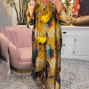 Floral V-neck yellow summer dress for women displayed on a mannequin in a stylish indoor setting, surrounded by modern furniture, including a chair and a couch, with a plant adding a touch of greenery.