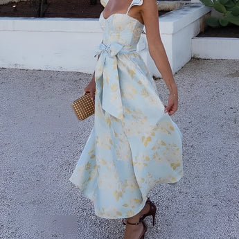 Floral vintage summer dress with sleeves in pastel blue and yellow, featuring a fitted waist and flowing skirt, modeled by a woman with visible shoulders and arms.