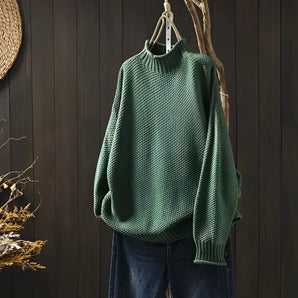 Forest green oversized knit sweater with a high collar and batwing sleeves hanging on a clothes hanger.