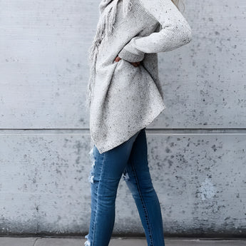 A woman wearing a fringed gray Bohemian wool cowl neck sweater with long sleeves and chic winter knitwear style.