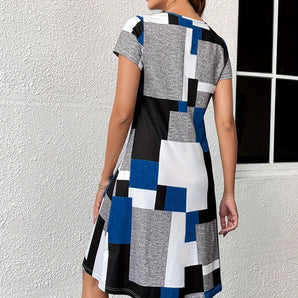 Geometric block print knee-length dress in blue, black, and white, featuring short sleeves and a round neckline, displayed against a minimalist background.