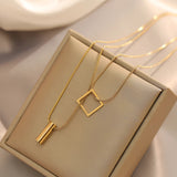 Elegant minimalist necklace with geometric gold bar and square pendant displayed on a white and brown background.
