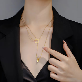 A woman wearing a geometric gold bar and square pendant necklace, elegantly styled against a dress shirt.