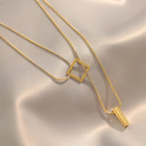 Elegant minimalist necklace with geometric gold bar and square pendant on a delicate chain displayed against a neutral background.