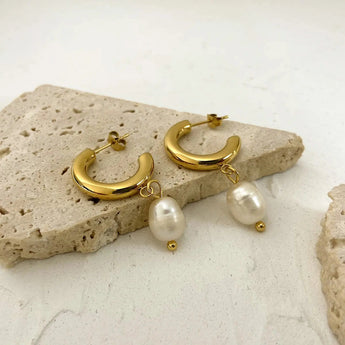 Gold Crescent Pearl Drop Earrings with elegant pearl accents and modern design, displayed on a beige wood background.