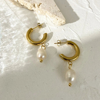 Gold crescent pearl drop earrings with delicate chain and circular design, featuring natural beige pearls and gold metal accents.