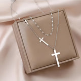 A minimalist, layered gold cross pendant necklace displayed on a wooden surface, adjustable with a sleek design.