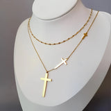 A minimalist gold cross pendant necklace featuring a layered design, worn around the neck, displayed against a white background.
