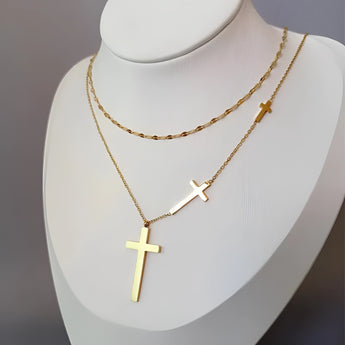 A minimalist gold cross pendant necklace featuring a layered design, worn around the neck, displayed against a white background.