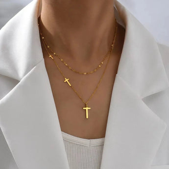 Gold cross pendant necklace with layered, minimalist design, worn on a woman's neck.