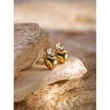 Gold crystal heart stud earrings, 18K plated, displayed on a wooden surface, close-up view.