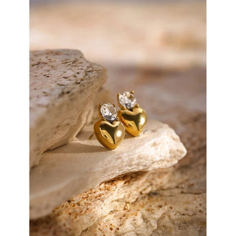 Gold crystal heart stud earrings, 18K plated, displayed on a wooden surface, close-up view.