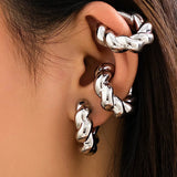 Close-up of a woman's ear wearing metallic silver gold diamond-studded hoop earrings with a twisted chain design, highlighting her facial features like nose, cheek, and jaw.