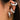 Close-up of a woman's ear wearing metallic silver gold diamond-studded hoop earrings with a twisted chain design, highlighting her facial features like nose, cheek, and jaw.