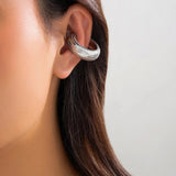 Silver huggie hoop earrings with pave setting, adorned with diamonds, worn on the ear of a woman.