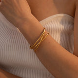 Gold heart bracelet worn on wrist, featuring an adjustable minimalist open heart design, shown on an arm with beige sleeve.