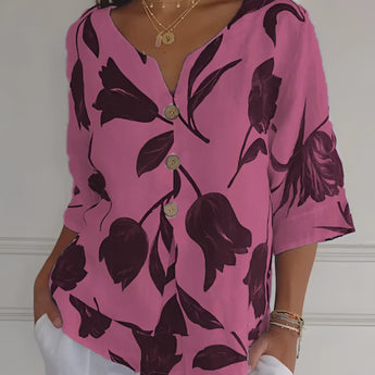 A woman wearing a pink dress accessorized with a gold layered coin pendant necklace, featuring detailing charms on a thin chain. The outfit complements the necklace, creating a chic and elegant look.
