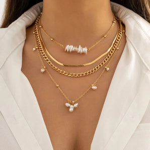 A set of gold layered necklaces with a pearl pendant, featuring a chunky chain and stylish chokers, worn on a woman's neck and chest area.