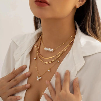 Woman wearing a set of gold layered necklaces with a pearl pendant, featuring chunky chains and stylish chokers.