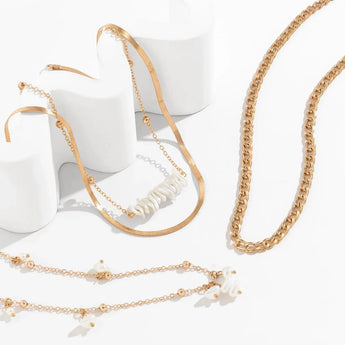 Gold layered necklaces set with pearl pendant, featuring a chunky chain and stylish chokers, displayed against a neutral background.