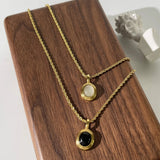Gold locket necklace with black onyx and white stone displayed on a wooden background.