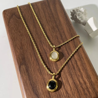 Gold locket necklace with black onyx and white stone displayed on a wooden background.