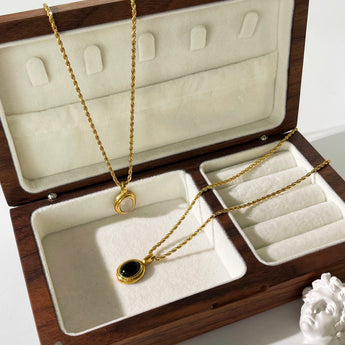 Gold locket necklace featuring black onyx and white stone in a two-tone design, displayed on beige background.