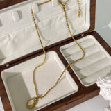 Gold locket necklace with black onyx and white stone in two-tone design on a beige background.