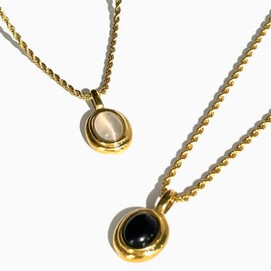 Gold locket necklace with black onyx and white stone, featuring a two-tone design, displayed against a neutral background.