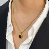 Gold locket necklace featuring black onyx and white stone, displayed on a mannequin's neck with a blazer backdrop.