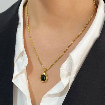 Gold locket necklace featuring black onyx and white stone, displayed on a mannequin's neck with a blazer backdrop.
