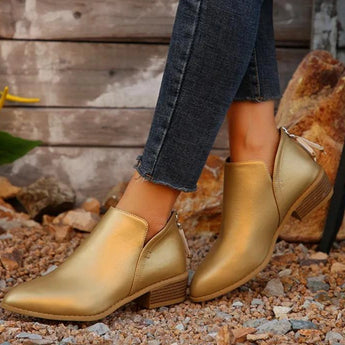 Gold metallic pointed toe ankle boots with a zipper, featuring a low heel design. The boots are showcased on a model's legs, highlighting their fashionable appearance suitable for both casual and dressy occasions.