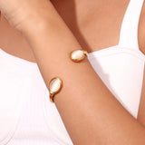 A woman's wrist adorned with a Gold Pink Cabochon Bracelet, showcasing luxury designer jewelry against her hand and arm.