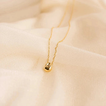 Gold stainless steel minimalist pendant necklace, hypoallergenic and tarnish-resistant, showcased on a beige fabric background.
