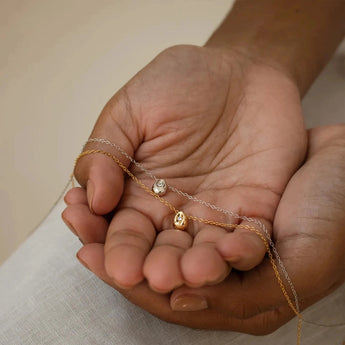 A minimalist gold stainless steel pendant shown on a hand, highlighting its hypoallergenic and tarnish-resistant properties, with a simple and elegant design complemented by a dress in the background.