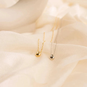 Gold stainless steel minimalist pendant necklace, hypoallergenic and tarnish-resistant, displayed on a natural material background.