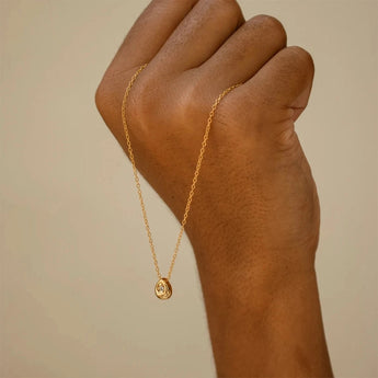 Close-up of a person's hand and wrist wearing a minimalist gold stainless steel pendant, showcasing its hypoallergenic and tarnish-resistant properties.