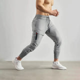A man standing and wearing gray tapered joggers, lightweight athletic sweatpants, showcasing a casual and sporty look.
