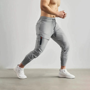 A man standing and wearing gray tapered joggers, lightweight athletic sweatpants, showcasing a casual and sporty look.