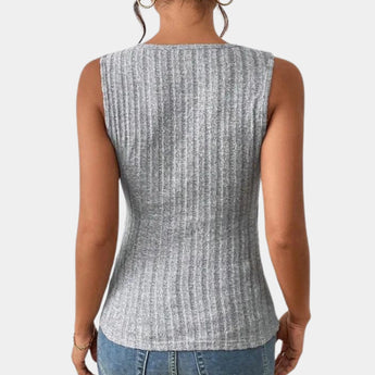 A woman wearing a gray ribbed sleeveless tank top with a deep V-neck and button details, paired with jeans.