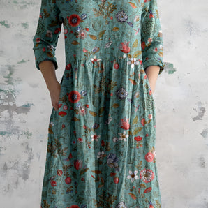 Green bohemian floral maxi dress with long sleeves, a V-neckline, and an empire waist, featuring a vibrant print with shades of azure, pink, and aqua.