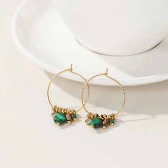 Gold hoop earrings with green crystal accents, designed by YA-CHAN, displayed against a minimalistic background.