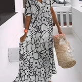 A woman wearing a green floral bohemian maxi dress with pockets, featuring a V-neck and short sleeves. The dress is styled for resort wear and is designed in a relaxed, flowing fit.